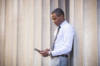 Black businessman leaning on wall using digital tablet