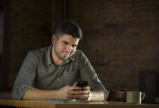 Caucasian man drinking coffee in cafe holding cell phone