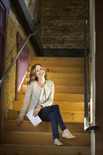 Caucasian woman holding paperwork sitting on wooden staircase