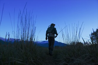 Caucasian man carrying fishing rod in field at dawn