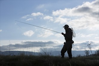 Silhouette of Caucasian man carrying fishing rod in field