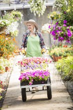 Caucasian woman pushing cart of potted plants in greenhouse