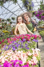 Caucasian grandmother and granddaughter pushing cart of potted plants in greenhouse