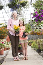 Caucasian grandmother and granddaughter holding potted plants in greenhouse