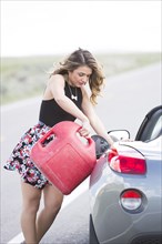 Caucasian woman pouring fuel from gas can into sports car