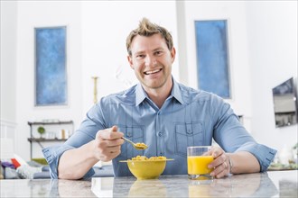 Caucasian man eating cereal in kitchen