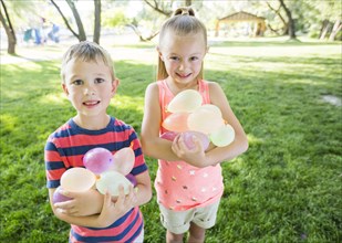 Caucasian brother and sister holding water balloons