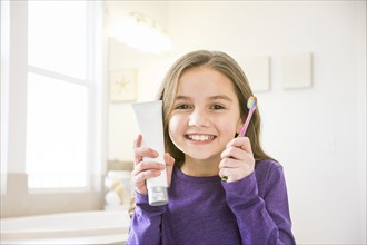 Smiling Caucasian girl holding toothbrush and toothpaste tube in bathroom