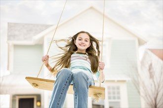 Caucasian girl on rope swing near house