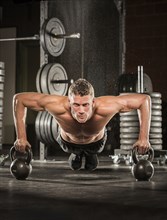 Caucasian man doing push-up using kettlebells in gymnasium