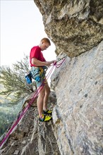 Caucasian man adjusting rope while rock climbing