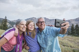 Caucasian grandparents and granddaughter posing for cell phone selfie
