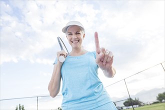 Caucasian woman holding tennis racket gesturing number one