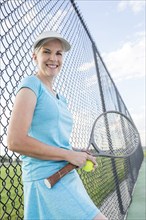 Caucasian woman holding tennis racket leaning on fence
