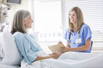 Caucasian nurse talking with woman in hospital bed