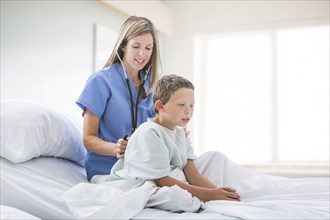 Caucasian nurse listening to chest of boy in hospital bed