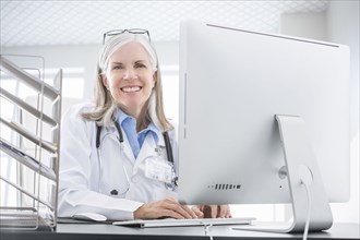 Smiling Caucasian doctor using computer at desk