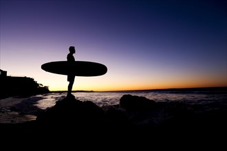 Silhouette of Hispanic man holding surfboard at beach