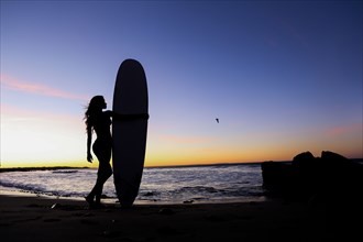 Silhouette of Caucasian woman holding surfboard at beach