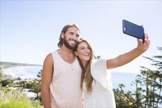 Caucasian couple posing for cell phone selfie at beach