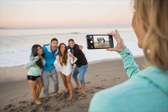Woman photographing friends at beach with cell phone