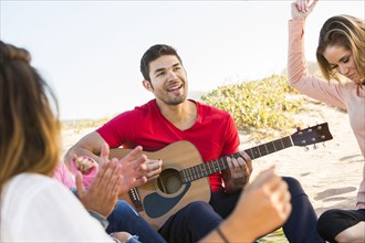 Man playing guitar for friends at beach