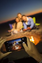 Hands of woman photographing friends on beach with cell phone