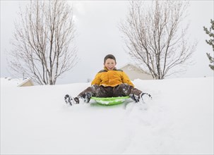 Smiling boy sliding on toboggan on hill in winter
