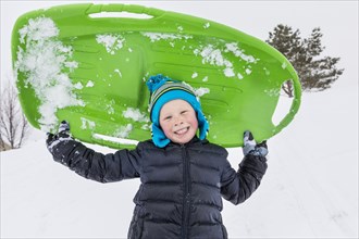 Smiling boy posing with toboggan in winter
