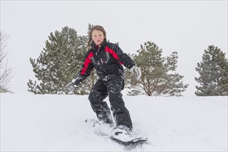 Serious girl riding snowboard on hill in winter