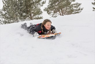 Smiling girl sliding on snowboard on hill in winter