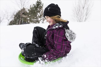 Smiling girl sliding on toboggan in snow