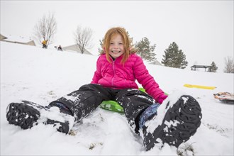Smiling girl sitting on toboggan in snow