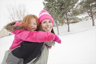 Smiling mother carrying daughter piggyback in winter