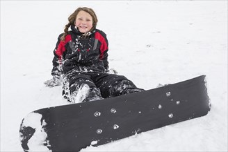 Smiling girl sitting in snow with snowboard
