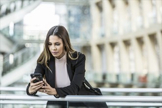 Mixed Race businesswoman texting on cell phone leaning on railing in lobby