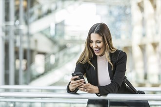 Mixed Race businesswoman texting on cell phone leaning on railing in lobby