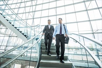 Smiling Mixed Race businessmen descending staircase