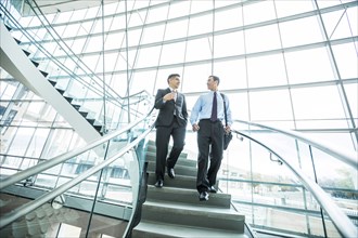 Smiling Mixed Race businessmen descending staircase and talking