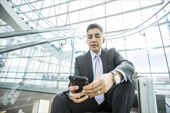 Serious Mixed Race businessman sitting on staircase texting on cell phone