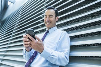 Smiling Mixed Race businessman leaning on wall texting on cell phone