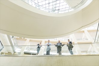 Portrait of smiling business people leaning on railing in lobby