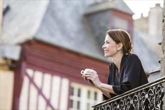 Caucasian woman drinking coffee on balcony in city