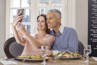 Caucasian couple posing for cell phones selfie in restaurant