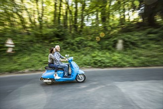 Caucasian couple riding blue motor scooter