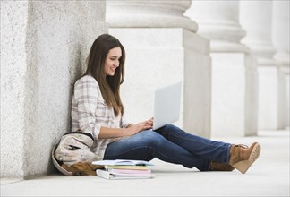 Caucasian woman leaning on pillar using laptop