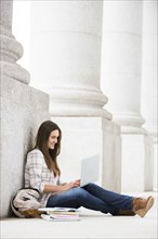 Caucasian woman leaning on pillar using laptop