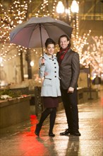 Caucasian couple carrying umbrella in city at night