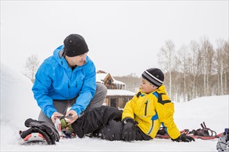 Caucasian father adjusting snowshoe for son