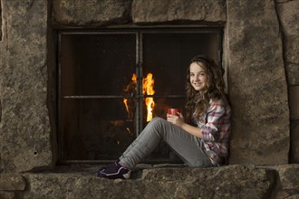 Smiling Caucasian girl sitting near fireplace